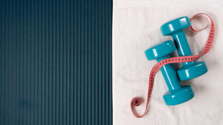 Measuring tape centimeter with dumbbells and towel on the mat for training - sports background with space for textの写真素材