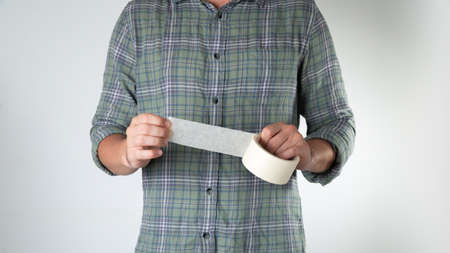 A man tears off a ribbon of white wide tape on a white backgroundの写真素材