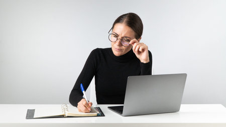 A serious businesswoman works in the office on a laptop, takes notes in a notebook