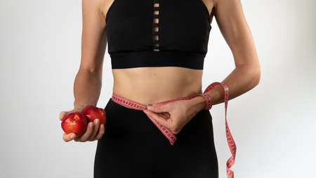 Weight loss, nutrition and sports - a woman with fruits measures her waistの写真素材