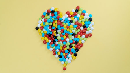 Heart of sweet multi-colored dragees on a yellow background