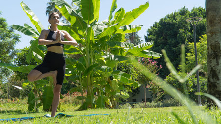 A woman does yoga in the park, stands in a pose on one leg. high quality photoの写真素材