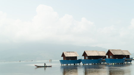 A fisherman in a boat sails away from the bungalowの写真素材