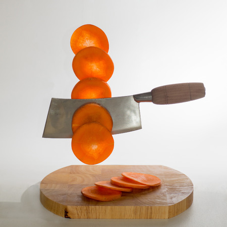 Chinese cleaver cutting carrots in the air on a white backgroundの写真素材