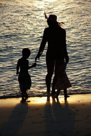 silhouettes of mother and two kid on sunset sea backgroundの写真素材