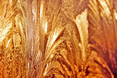 Icy frosty ornate pattern of thin ice on the window at sunset.