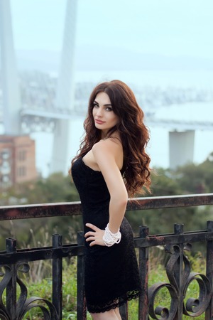 Portrait of young woman with long curly hair wearing little black dress in urban backgroundの写真素材