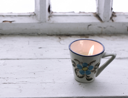 Small lit candle in cup with flowers on window closeupの写真素材