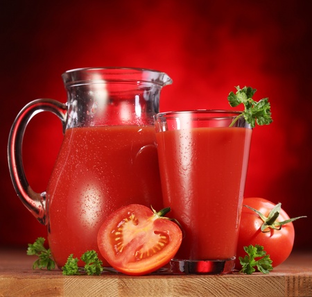 Still life: tomatoes, jug and glass full of fresh tomatoes juice on wooden table.の写真素材