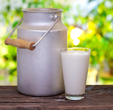 Milk in aluminum can and glass on the old wooden table on outdoor setting.の写真素材