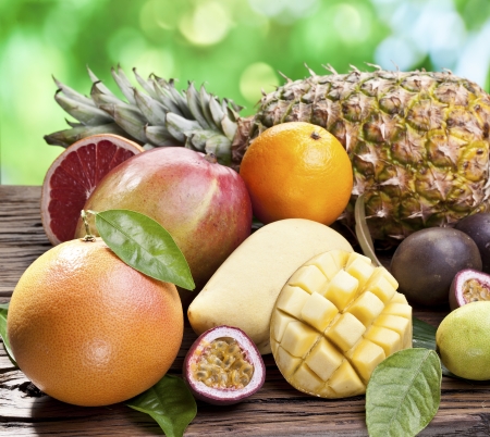 Exotic fruits on a wooden table with green foliage on the background.の写真素材