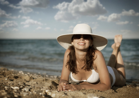 Young woman in white swimsuit sunbathes sitting on sunbed.の写真素材