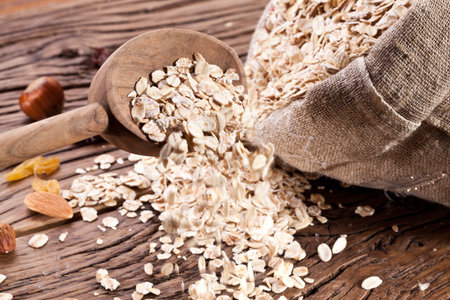 Rolled oats in the wooden spoon and sackon old wooden table.