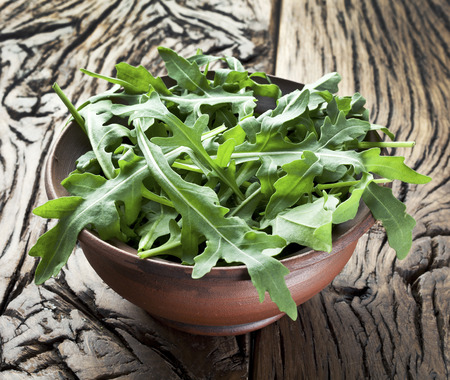Green arugula leaves in the plate on a wooden table.の写真素材