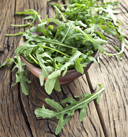 Green arugula leaves in the plate on a wooden table.の写真素材