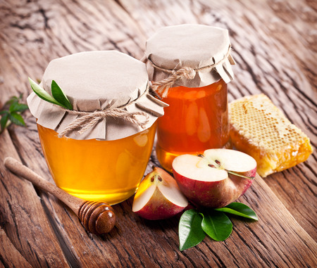 Glass cans full of honey, apples and combs on old wooden table.の写真素材