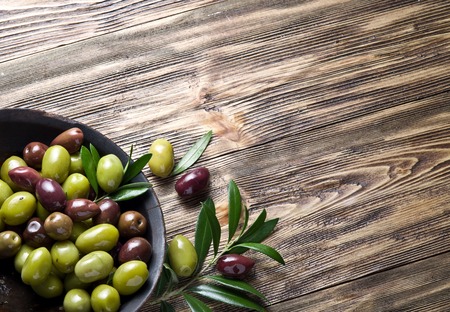 Wooden bowl full of olives and olive twigs besides it.の写真素材