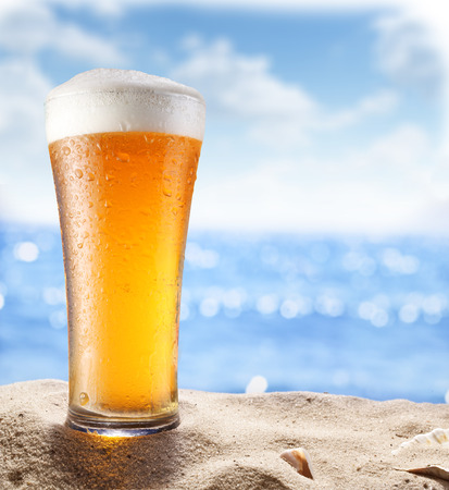 Ice beer glass in the sand. Blurred sea at the background.の写真素材