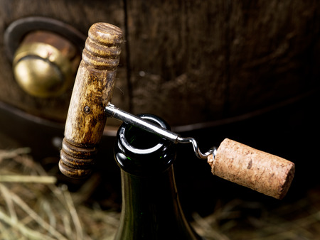 Opening of a wine bottle with corkscrew with wooden barrel on the background.の写真素材