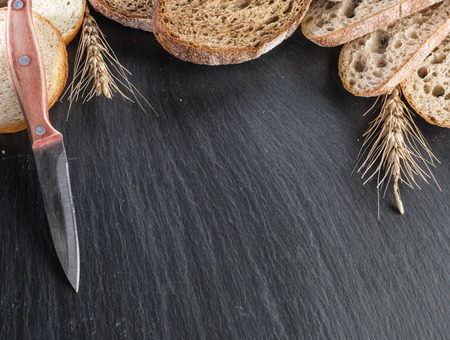 Bread slices, a wheat and a knife on the black stone desk.の写真素材
