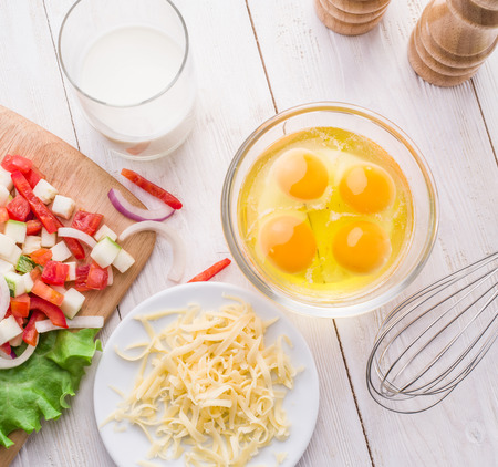 Omelette ingredients: eggs, fresh cut vegetables, milk and cheese on the wooden table.の写真素材