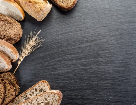 Bread slices, a wheat and a knife on the black stone desk.の写真素材