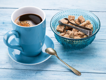 Cup of coffee and cane sugar cubes on old blu wooden table.の写真素材