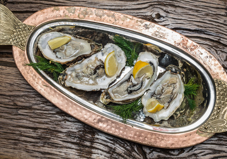 Opened oysters with piece of lemon on the cooper tray.の写真素材