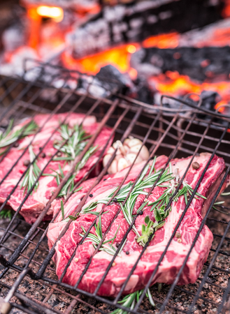 Rib eye steaks and grill with burning fire behind them.の写真素材