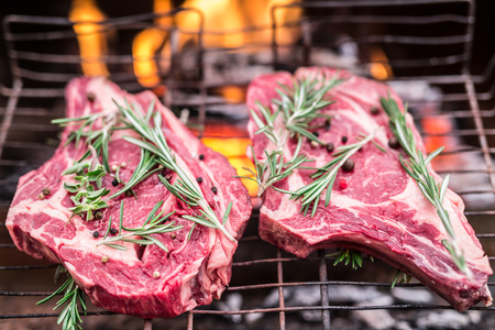 Rib eye steaks and grill with burning fire behind them.の写真素材