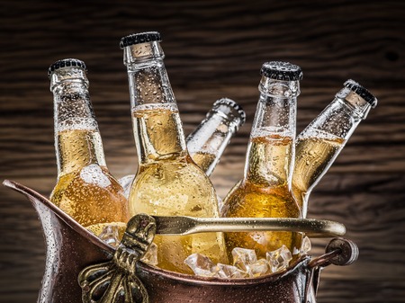 Cold bottles of beer in the brazen bucket on the wooden table.の写真素材