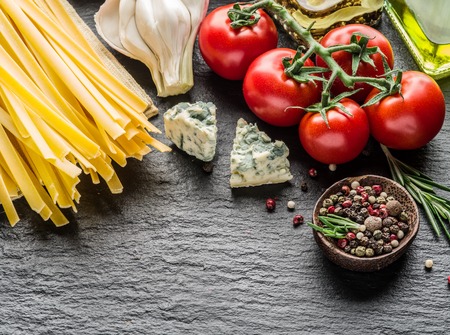 Pasta ingredients. Cherry-tomatoes, spaghetti pasta, rosemary and spices on a graphite board.の写真素材