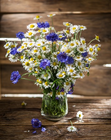 Bouquet of chamomiles and cornflowers in the vase on the wooden table.の写真素材