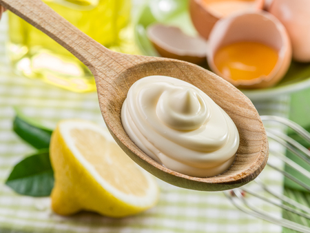 Natural mayonnaise sauce in the wooden spoon and its ingredient on the background.の写真素材