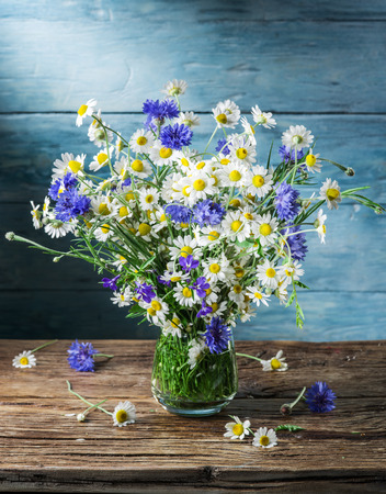 Bouquet of chamomiles and cornflowers in the vase on the wooden table.の写真素材