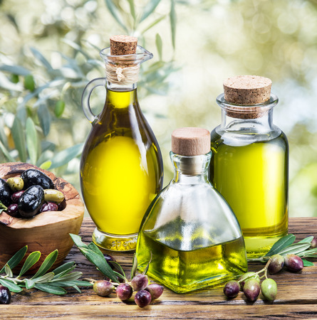 Olive oil and berries are on the wooden table under the olive tree.の写真素材