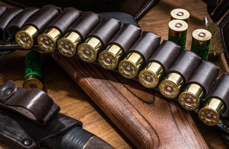 Hunting equipment - pump action shotgun, 12 guage cartridge end hunting knife on the wooden table.
