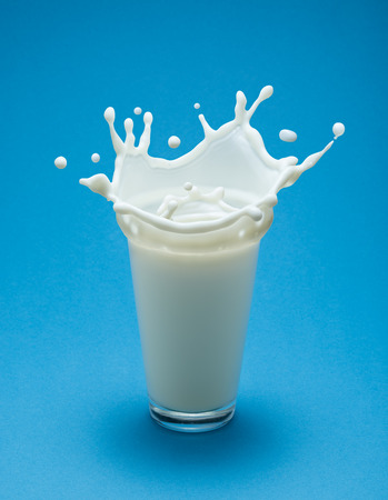 Glass of milk and milk splash. Blue background.の写真素材