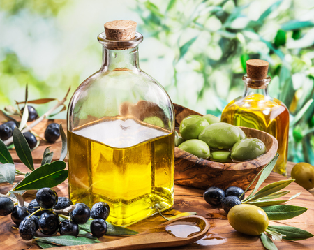 Olive oil and berries are on the wooden table under the olive tree.の写真素材