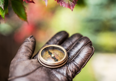 Man's hand in a leather glove holding a compass. Nature background.の写真素材