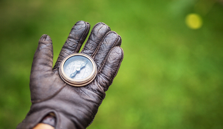 Man's hand in a leather glove holding a compass. Nature background.の写真素材