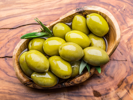Whole table olives in the wooden bowl on the table. Top view.の写真素材