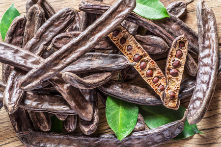 Carob pods and carob beans on the wooden table.の写真素材