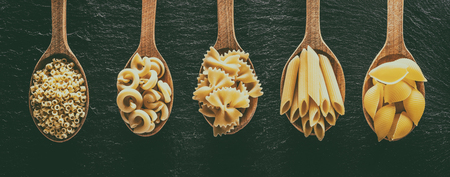 Different pasta types in wooden spoons on the table. Top view.の写真素材