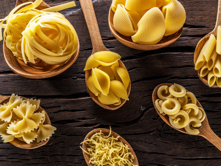 Different pasta types in wooden spoons on the table. Top view.の写真素材