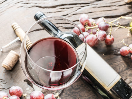 Wine glass, wine bottle and grapes on wooden background.
