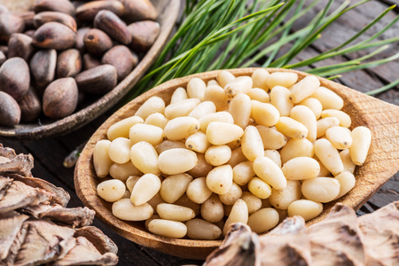 Pine nuts in the spoon and pine nut cone on the wooden table. Organic food.の写真素材