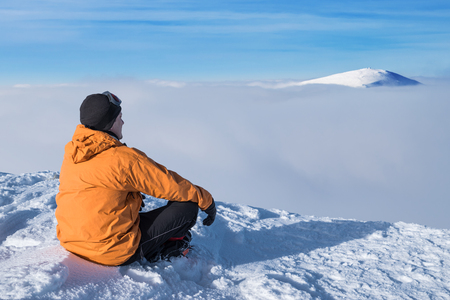 Winter hiking. Tourist on snowy mountain top enjoying beautiful view of cloudscape.の写真素材