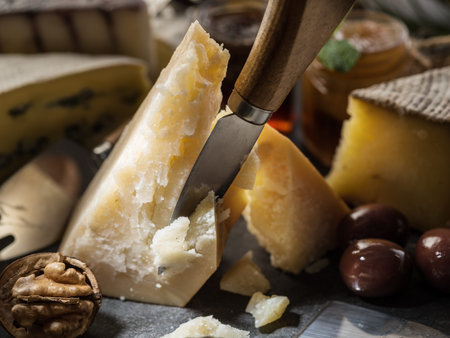 Piece of Parmesan cheese and assortment of different cheeses at the background.