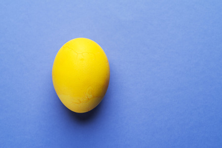 Stained in yellow Easter egg as an attribute of Easter celebration on blue background.の写真素材